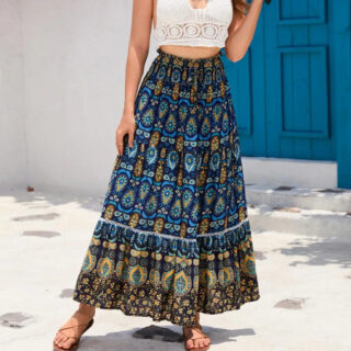 Photo d'une femme debout dent une porte bleue et portant une jupe bohème élégante longue bleue foncée imprimée et un crop top blanc