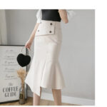 Photo d'une jeune femme debout portant une jupe sirène blanche asymétrique avec ceinture boutonnée devant et un top noir