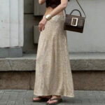 Photo d'une femme portant une jupe sequins longue et fluide dorée avec des sandales et un sac à l'épaule, marchant dans la rue