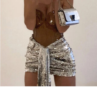 Photo montrant une jeune femme habillée d'une mini jupe drapée à paillettes argentée un haut brillant et un petit sac argenté