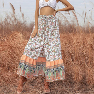 Photo d'une jeune femme debout dans la campagne portant une jupe longue bohême imprimée fendue et fermée par boutonnage simple et un crop top blanc