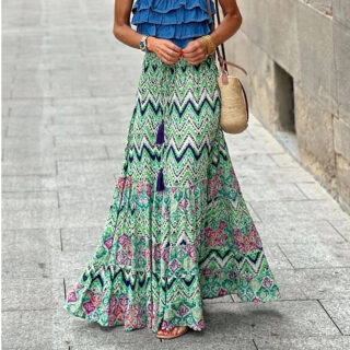 Photo d'une jeune femme marchant dans la rue et portant une jupe longue style bohême à motifs géométriques verte avec un haut bleu foncé et un sac en raphia en bandoulière