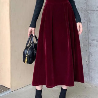 Photo d'une jeune femme debout portant une jupe trapèze bordeaux, un sac à main noir, des boots noires et un pull à manches longues noir