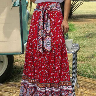 Photo d'une femme debout devant une caravane portant une jupe bohème rouge imprimée avec écharpe nouée sur la taille