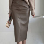 Jupe crayon longue marron porté avec un pull beige. La femme porte un journal