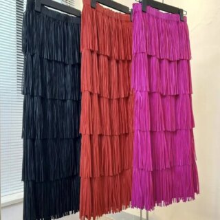Photo montrant trois jupes longues à plusieurs rangées de franges sur cintres une noire, une rouge et une rose