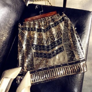 Photo d'une mini-jupe à paillettes sequins noirs et dorés, accrochée sur une cintre, posé sur un canapé en cuir noir avec une paire d'escarpins doré à côté.