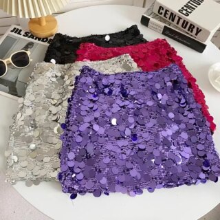Photo de plusieurs mini jupes à sequins placée les unes sur les autres sur une table avec une petite lampe et des livres.