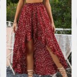 Jupe asymétrique imprimé floral rouge. Porté par une femme debout avec des sandalles blanches