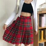 Femme portant une jupe plissée écossaise avec un haut noir et une veste blanche.