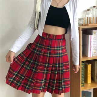 Femme portant une jupe plissée écossaise avec un haut noir et une veste blanche.
