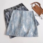 Photo de plusieurs mini jupe en jean à sequins disposées les unes sur les autres à côté d'un sac en cuir camel