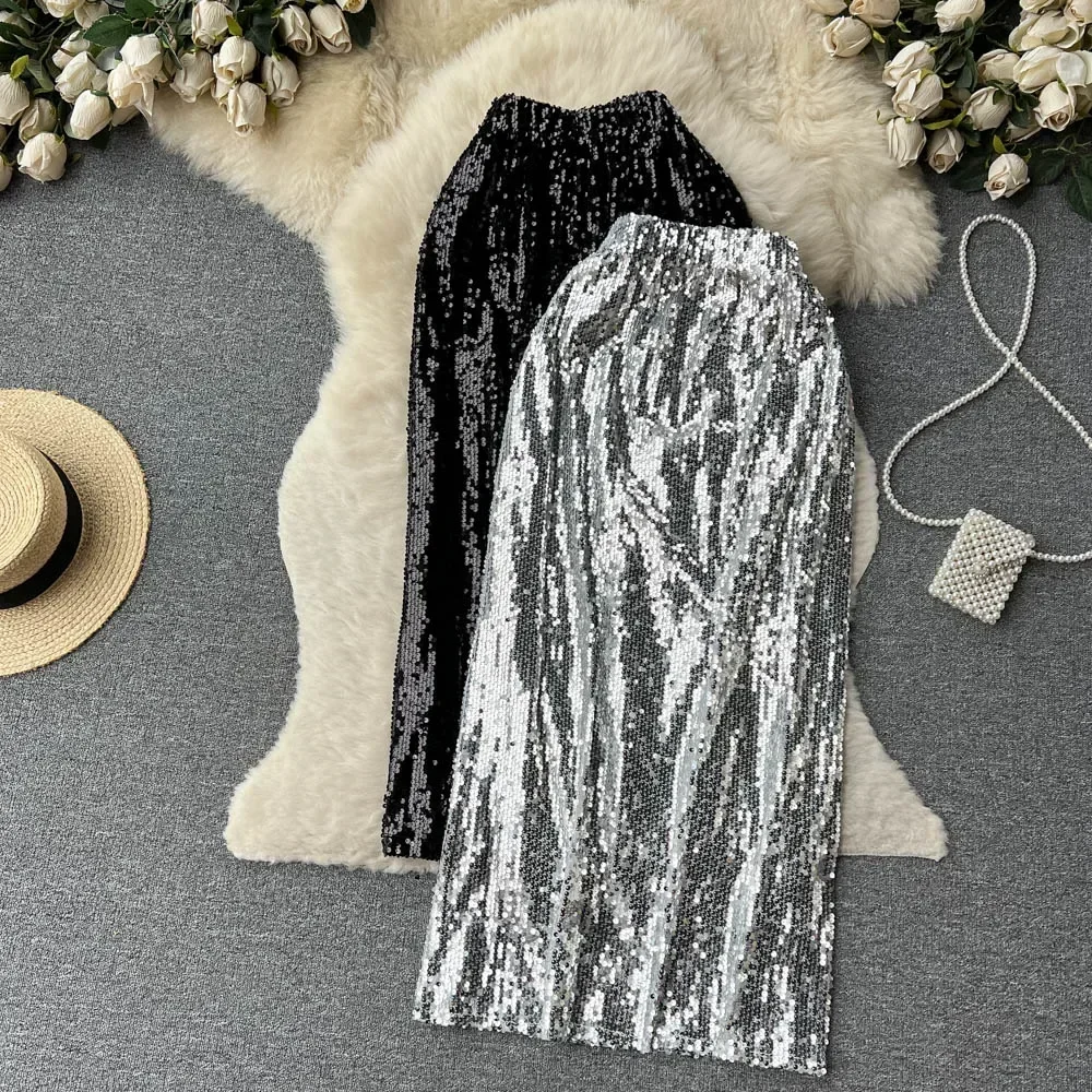 12176-bfvqfn.jpg Photo de deux jupes à sequins taille haute élastique, une argente sur une noir, sur un tapis en poils blanc à côté d'un chapeau de paille et d'un sac à main.
