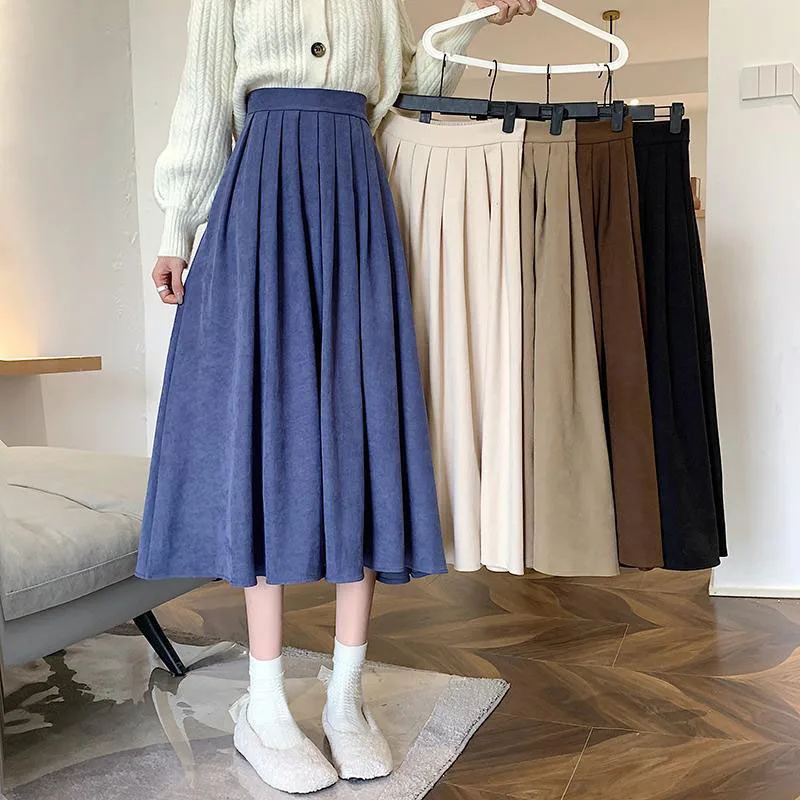 Photo d'une jeune femme portant une jupe trapèze bleue plissée avec des baskets et chaussettes blanches devant un portant avec quatre autres jupes de couleur différente