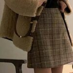 Jupe de tailleur courte à carreaux marron,portée par une femme qui porte un sac sur le côté