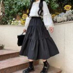 Jupe mi-longue à volants noire portée avec un chemisier blanc et des chaussures noires