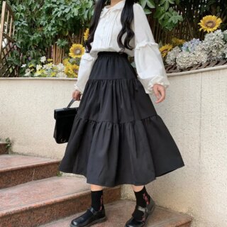 Jupe mi-longue à volants noire portée avec un chemisier blanc et des chaussures noires