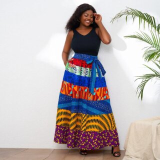 Photo d'une jeune femme debout devant un mur blanc portant une jupe wax colorée à tendance bleue avec un débardeur noir et des chaussures à petits talons noirs