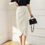 Photo d'une jupe tulipe droite drapée taille haute blanche portée par une femme avec un haut noir et un petit sac à main