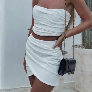 Photo d'une femme portant une jupe tulipe blanche avec un haut bustier assorti et un sac à main pochette à chaine noir sur l'épaule en se tenant la hanche.