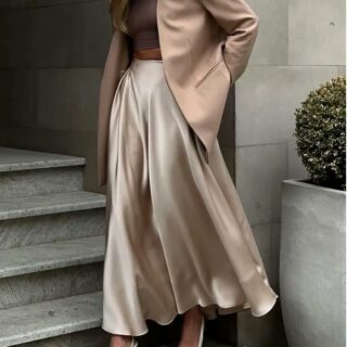 Photo d'une femme marchant devant un escalier et portant une jupe champagne en soie avec un blazer marron clair la main droite sur la hanche