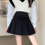 Jupe de grossesse plissée courte noire. portée avec un pull blanc