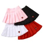 Sur fond blanc, on voit quatre jupes plissées pour petite fille. Elles sont rose, noire, blanche et rouge.
