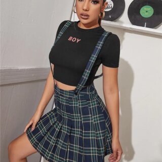 Photo d'une jeune femme debout une jambe sur une marche de trois quart profil portant un jupe salopette écossaise bleue et un tee-shirt noir