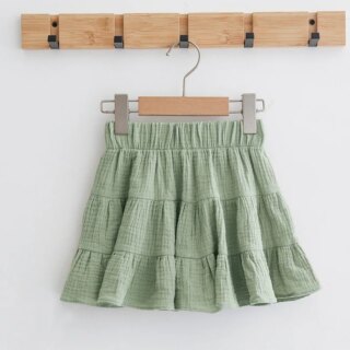 On voit une jupe vert d'eau à volants pour petite fille. Elle est suspendue à un cintre en bois;