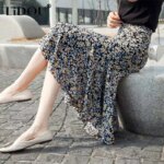 Femme portant une jupe longue avec des fleurs et étant assise sur un banc.
