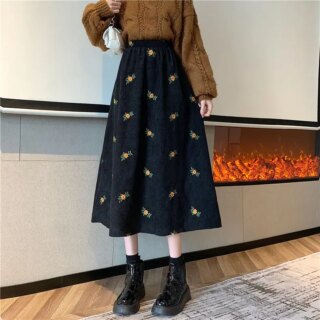 Femme portant une jupe longue noire, un pull marron et des bottines.