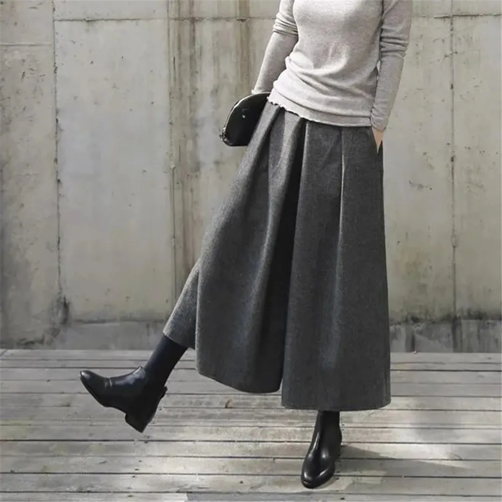 Photo d'une jeune femme qui avance une jambe et porte une jupe culotte gris foncée ressemblant à de la laine, un pull gris clair et des bottines noires avec un petit sac noir