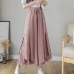 Photo d'une jeune femme près d'un fauteuil en bois portant une jupe culotte rose plissée avec petit noeud à la taille