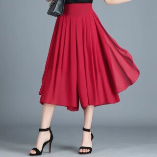 Photo d'une femme portant une jupe culotte rouge plissée mi longue à taille haute avec des sandales à talons et un petit sac sur l'épaule