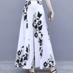 Photo représentant une jupe culotte longue blanche à fleurs portée par une femme avec une pochette dans la main gauche et des sandales noires à talons hauts
