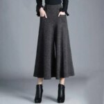 Photo représentant une jupe culotte mi-longue gris foncé sur une jeune femme qui porte des bottines et un pull noir et a ses mains dans les poches de la jupe culotte