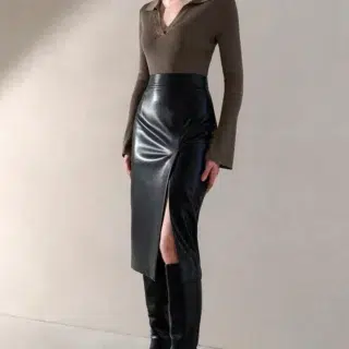 Photo d'une jeune femme portant une jupe noire en simili cuir fendue sur le côté gauche avec des bottes noires et un body kaki