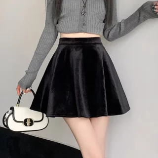 Photo d'une jeune femme portant une jupe patineuse mini noire en velours , un top gris à manches longes et un petit sac blanc et noir dans la main droite