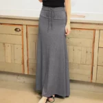 Photo d'une femme portant une jupe longue fluide gris foncé avec un lien noué à la taille debout devant un buffet beige