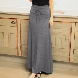 Photo d'une femme portant une jupe longue fluide gris foncé avec un lien noué à la taille debout devant un buffet beige