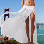 Photo d'une jeune femme debout devant un pont portant une jupe de plage blanche longue taille basse fendue jusqu'en haut