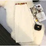Photo d'une jupe blanche en velours côtelé à fente devant et ceinture marron posée sur un plaid de fausse fourrure blanc avec un sac noir à bandoulière et un magazine ouvert à côté