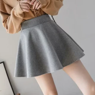 Photo d'une jeune fille sur un fond gris clair portant une jupe patineuse gris se et un haut marron à manches longues