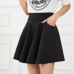 Photo d'une jeune femme portant une jupe patineuse noire avec la main gauche dans la poche et un tee-shirt blanc imprimé noir