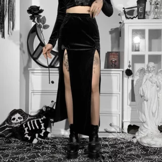 Phoro d'une femm eportant une jupe mi-longue noire fendue devant des deux côtés taille haute avec des bottines noires et un top noir manches longues dans un décor noir et blanc