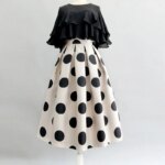 On voit une tenue sur un mannequin : une jupe blanche à pois noirs et un top à volants noirs. C'est une tenue rétro.