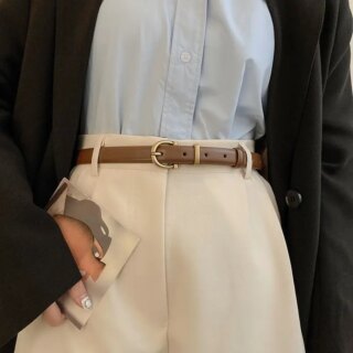 Photo d'une ceinture fine marron portée sur un pantalon beige avec une chemise bleu et une veste noir.