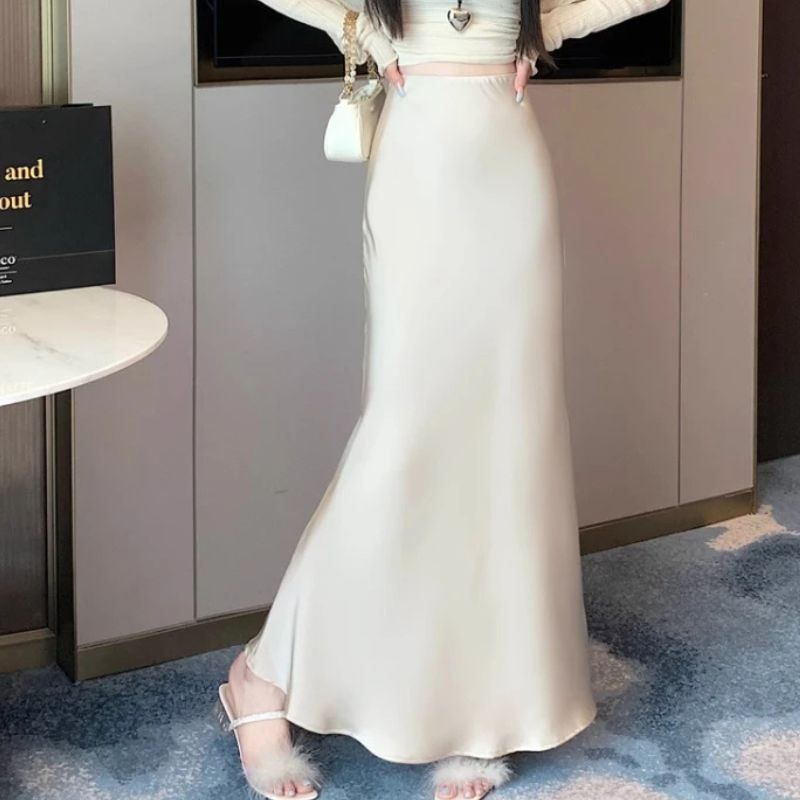 Jupe Satinée Moulante et Raffinée portée par une femme avec un sac sur le bras et une table à gauche